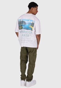 White oversized t-shirt featuring a colorful landscape graphic on the back, paired with olive cargo pants and white sneakers.