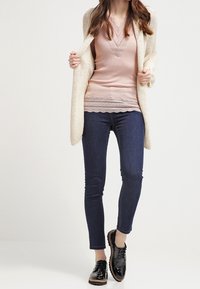 Krémový pletený kardigan, růžový žebrovaný top s krajkovým lemem, tmavé úzké džíny a černé lakované kožené boty s texturovanou podrážkou.