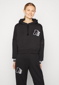 Black cropped hoodie with a hood, drawstrings, and embroidered logo detail. Paired with matching black pants featuring similar accents.