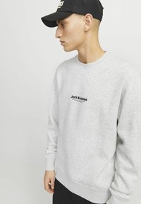 Sweatshirt gris avec un col rond, des manches longues et une finition texturée. Présente un logo noir imprimé à l'avant.