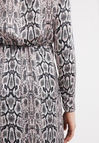 Abito a maniche lunghe in stampa pitone rosa e nero, con vita aderente e texture liscia. Il design enfatizza i dettagli del motivo squamato.