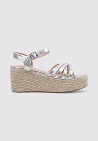 Sandalia cuña metálica plateada con tiras entrelazadas, hebilla ajustable en el tobillo y suela de plataforma de yute trenzado. Textura suave, diseño moderno.