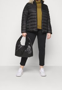 Giacca imbottita nera, dolcevita verde oliva, leggings neri, sneaker bianche e una borsa in pelle nera con maniglia curva.