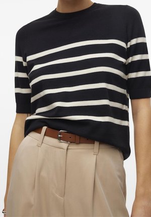 Person trägt ein schwarz-weiß gestreiftes kurzärmeliges Hemd, das in beige hoch taillierte Hose mit braunem Gürtel gesteckt ist.
