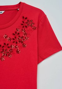 Top corto de manga corta rojo con cuello redondo, que presenta recortes de flores y bordado de lentejuelas rojas en el pecho.