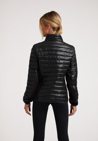 Giacca nera imbottita con colletto alto. Presenta una texture lucida e trapuntata e un tessuto opaco a contrasto sui lati. Design elegante e raffinato.