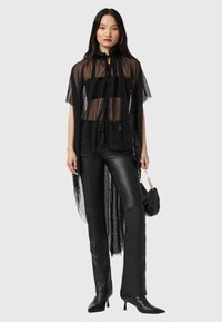 Czarna przezroczysta bluzka z krótkimi rękawami, ozdobiona rozproszonymi wzorami kropek. Do tego czarne skórzane spodnie i mała torebka.