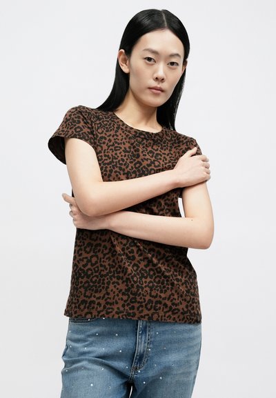 Καφέ μπλούζα με σχέδιο λεοπάρ, κοντά μανίκια, στρογγυλή λαιμόκοψη και απαλή υφή. Συνδυάζεται με ανοιχτόχρωμο μπλε τζιν με διακοσμητικά στοιχεία.
