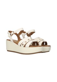 Witte wedge sandalen met meerdere smalle banden, decoratieve accenten in goudkleur, en een bruine binnenzool op een gladde beige platformzool.