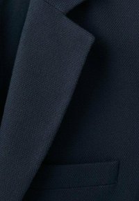 Marineblauer strukturierter Stoff mit einem subtilen gewebten Muster. Verfügt über ein scharf geschnittenes Revers und eine Tasche. Das Material wirkt robust, aber gleichzeitig flexibel.