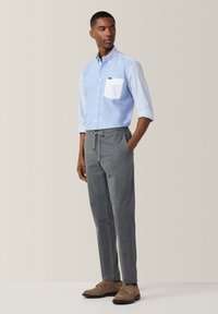 Camisa de botones a rayas azul claro con un bolsillo blanco, combinada con pantalones grises con cordón y zapatos de ante marrones. Estilo sencillo y casual.