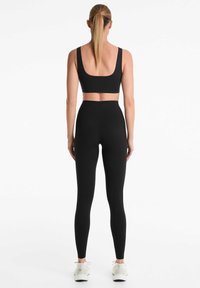 Soutien-gorge de sport noir avec larges bretelles associé à un legging noir taille haute. Texture de tissu lisse et coutures minimales. Des baskets blanches complètent le look.