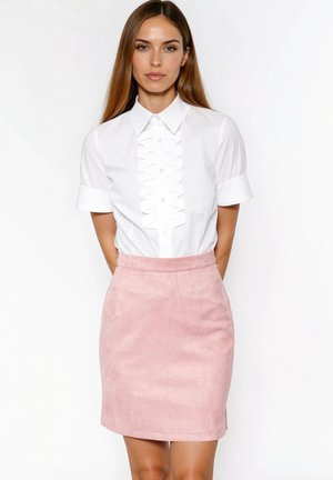 Biała koszula z kołnierzykiem i falbankami z tkaniny na przodzie, zestawiona z miękką, różową mini spódniczką z ekologicznego zamszu z paskiem w talii i bezszwowym wykończeniem.