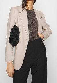 Beige blazer med skräddarsydd design, i kombination med en texturerad brun topp och svarta byxor med hög midja. Innehåller en lurvig svart väska.