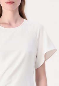 Biely krátky rukáv top s okrúhlym výstrihom a hladkým, mäkkým materiálom. Obsahuje široké, voľné rukávy a uvoľnený strih.
