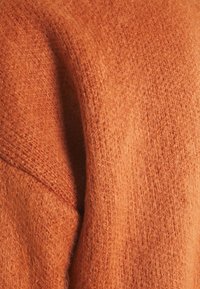 Pomarańczowa dzianina o miękkim, teksturowanym wykończeniu; charakteryzuje się luźnym splotem, tworząc przytulny wygląd.