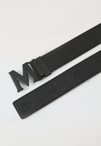 Svart läderbälte med matt yta, prytt med ett präglat logomönster och en glänsande, kantig 'M'-metallspänne.