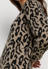 Maglione beige con un design a stampa leopardata nera, caratterizzato da un collo rotondo e maniche lunghe, realizzato in tessuto testurizzato.