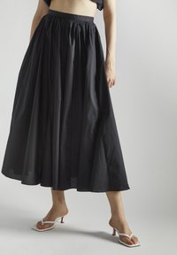 Falda negra de longitud hasta el tobillo con diseño plisado, hecha de una tela ligera. Presenta una cinturilla elástica y una textura suave.