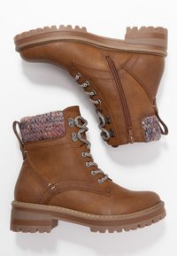 Bottes basses en cuir marron avec un col supérieur tricoté multicolore, des œillets métalliques, des lacets décoratifs et une semelle épaisse texturée avec des rainures.