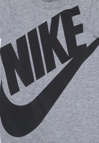 Grå bomulls-T-skjorte med en stor svart Nike-logo. Kort erme, rund hals, glatt tekstur, uten ekstra mønstre eller aksenter.