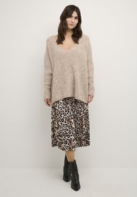 Beige gebreide trui met V-hals, gecombineerd met een geplooide rok met een luipaardprint in neutrale tinten, en zwarte puntige enkellaarsjes.