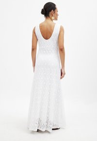 Witte kanten maxi-jurk met een U-vormige rug, mouwloos ontwerp, getailleerde corsage en uitlopende rok. Geweven bloemenpatroon over de gehele jurk.