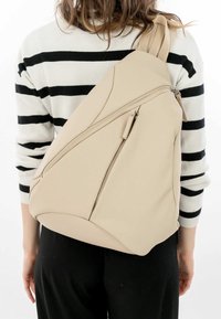 Beige axelremsrygga med en stilren design, tillverkad av syntetiskt material; har snedställda dragkedjefickor och en slät yta.