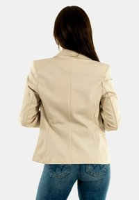 Beige fitted blazer with long sleeves, side pockets, and vertical seams. Paired with blue denim, showcasing a classic cut and casual style.