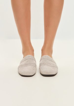 Geweven instap schoenen in lichtbeige met een gestructureerd detail en een platte bruine zool, met een vierkante neus en zonder zichtbare hardware.
