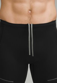 Sorte atletiske shorts med en tætsiddende design, med en grå snor, glat tekstur og en subtil prikket mønster på siderne.