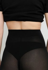 Leggings neri a vita alta con una texture liscia e pannelli semitrasparenti; dotati di una cintura spessa per supporto.