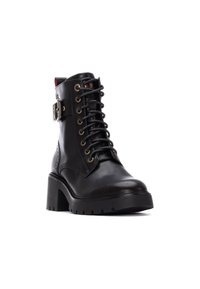 Botas de tobillo de cuero negro con cordones en la parte delantera, ojales dorados y un hebilla lateral. Presentan un tacón grueso y texturizado, y una suela resistente.
