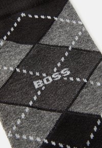 Gros plan sur un tissu à motif argyle gris et noir avec des lignes pointillées blanches et le mot "BOSS" tricoté au centre.