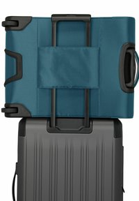 Twee stuks bagage op elkaar gestapeld. De bovenste is van teal stof met een gladde textuur en een in te klappen handvat. De onderkant is zwart, met een harde schaal en verticale groeven.