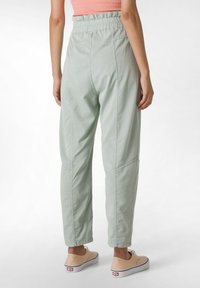  Lichtgroene, losvallende, elastische broek met zijnaad en taps toelopende enkels, gemaakt van een zachte, lichte stof.