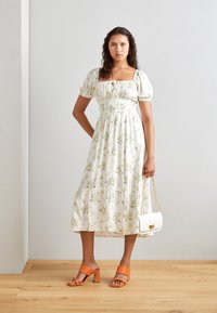 Bílá květinová midi šaty s nafouknutými rukávy a čtvercovým výstřihem; doplněné o oranžové sandály s blokovým podpatkem a bílou prošívanou kabelkou.