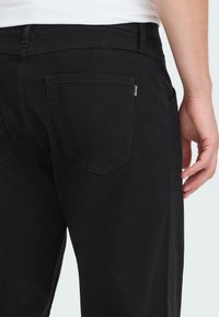 Zwarte spijkerbroek met een rechte snit. Voorzien van twee achterzakken, subtiele stiksels en een klein merklabel op de rechterzak.