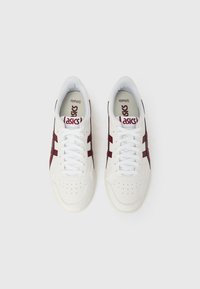 Valged tossud maroonsete aktsentide ja triipudega, kus on perforatsiooniga varbakast, valged paelad ja bränditud sisetallad. Siledast nahast tekstuur.