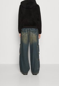 Giacca nera morbida con cappuccio abbinata a pantaloni cargo in denim blu oversize con numerose tasche e una finitura sbiadita.