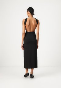 Melnā atpakaļ atvērtā kleita ar pieguļošu siluetu, mīkstu audumu, garu garumu un platām lencēm. Apvienota ar melnām augstpapēžu kurpēm ar svārkiem.