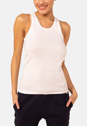 Weißes Baumwolltanktop mit Rundhalsausschnitt und breiten Trägern, das eine figurbetonte Passform hat. Glatte Textur; kombiniert mit dunklen Jogginghosen.
