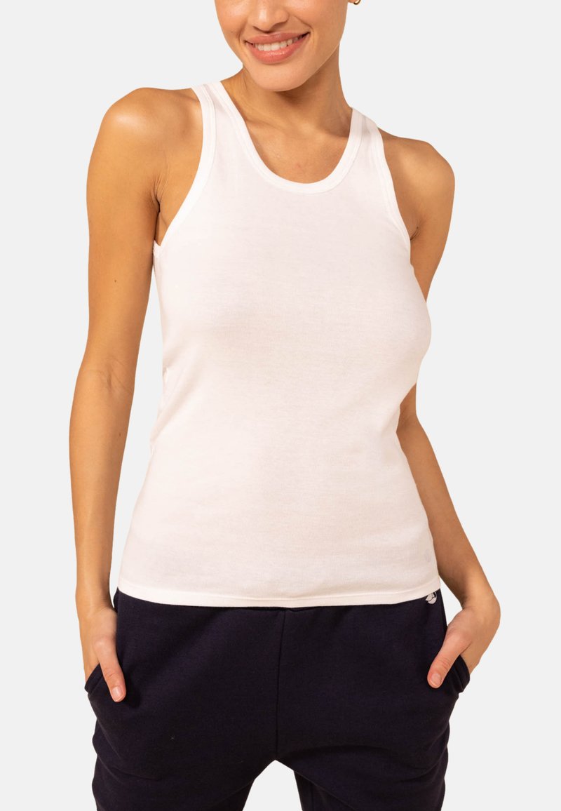 Weißes Baumwolltanktop mit Rundhalsausschnitt und breiten Trägern, das eine figurbetonte Passform hat. Glatte Textur; kombiniert mit dunklen Jogginghosen.