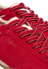 Zapatillas de ante rojo con detalles y cordones blancos. Presentan una superficie texturizada y detalles de costuras. Logo grabado en dorado en el lateral.