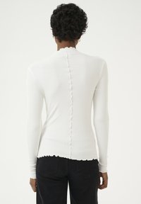 Vit ribbad långärmad topp med fransad bakseam och fåll. Avsmalnande design med en subtil textur, kombinerad med svarta jeans.