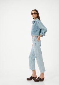 Chaqueta de mezclilla cortada de color azul claro con dobladillo deshilachado y bolsillos, combinada con jeans desgastados de tiro alto y zuecos de plataforma marrón oscuro.