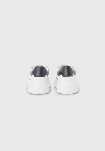 Baskets blanches avec accents noirs, design bas, cuir lisse, semelles texturées et détails de logo remarquables sur le talon.