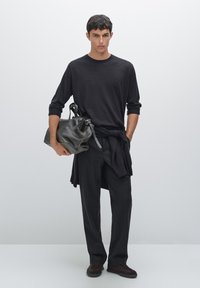 Czarna koszula z długim rękawem i spodnie, sweter dziany związany w talii, trzymający ciemną skórzaną torbę. Prosty, nowoczesny design i dopasowany krój.