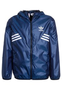 Merinoväri tuulenpitävä takki, joka on valmistettu kiiltävästä nailonista. Takissa on huppu, etuvetoketju ja valkoiset raidat olkapäillä.