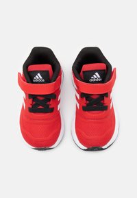 Baskets de sport rouges avec des accents noirs, tige en mesh, semelle blanche, lacets noirs et une fonctionnalité de sangle ajustable. Logo Adidas sur la languette.